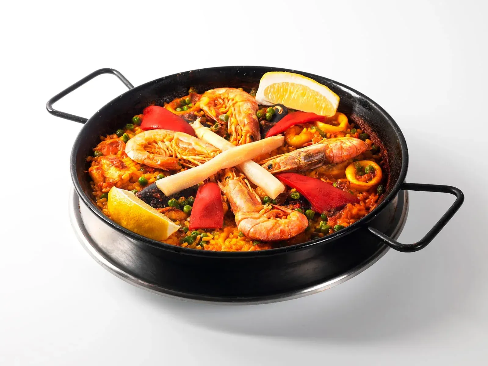 Paella negra con arroz, mariscos y verduras, adornada con rodajas de limón.