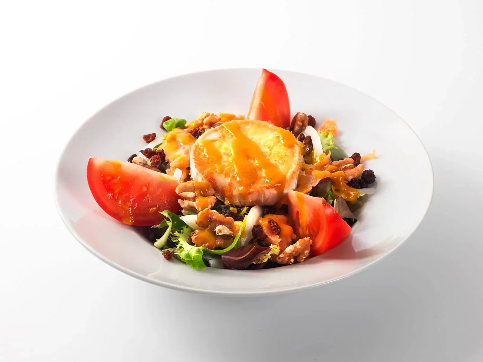 Mezcla colorida de frutas y ensalada en un tazón blanco, cubierta con rodajas de naranja y fresas.
