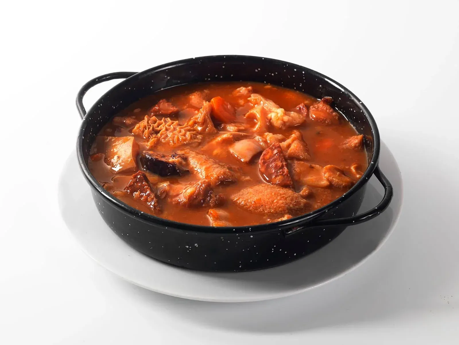Bol negro con guiso o sopa roja espesa sobre un fondo blanco.
