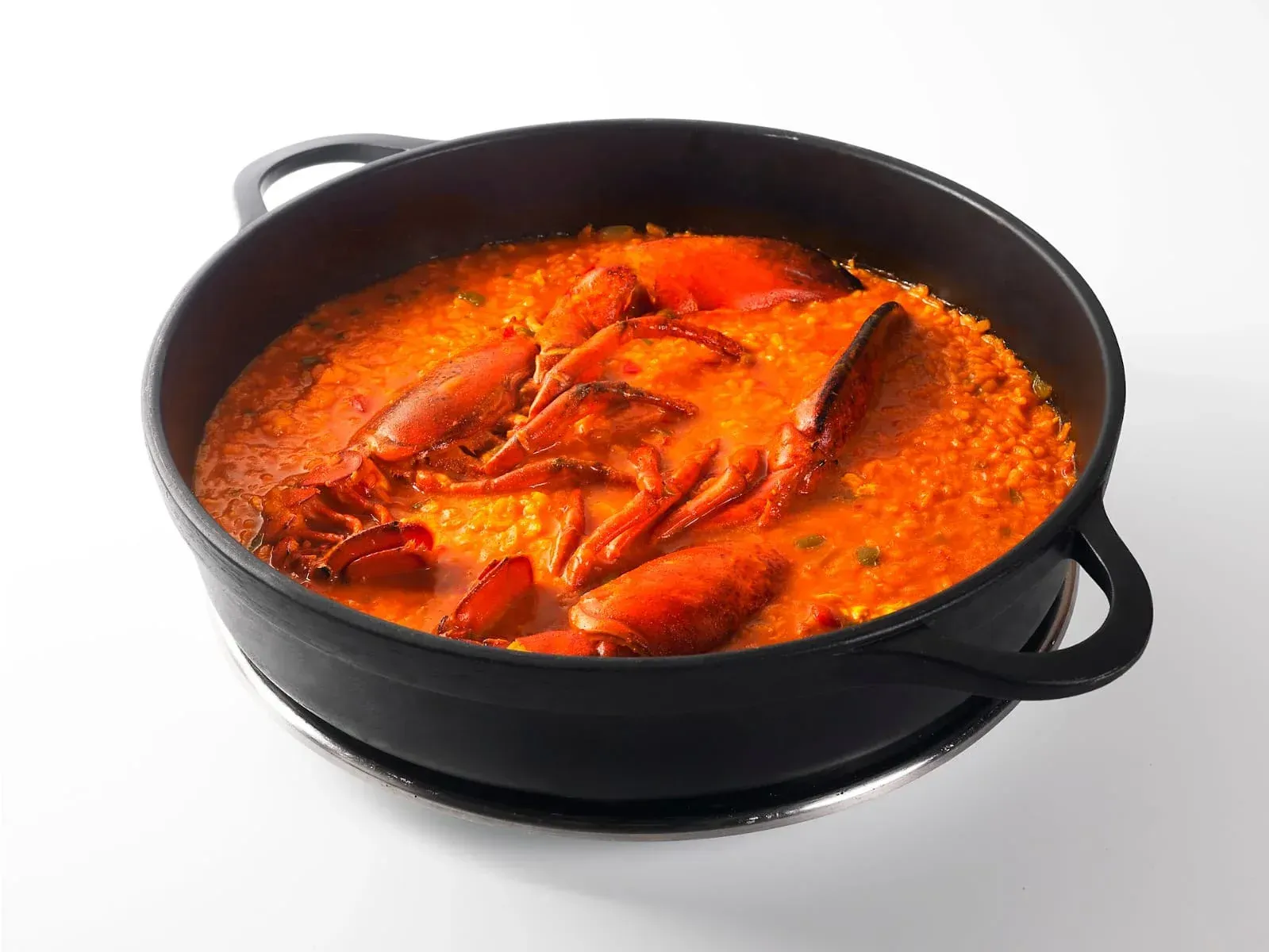 Olla negra con guiso de mariscos rojos y cáscaras de cangrejo sobre la estufa.