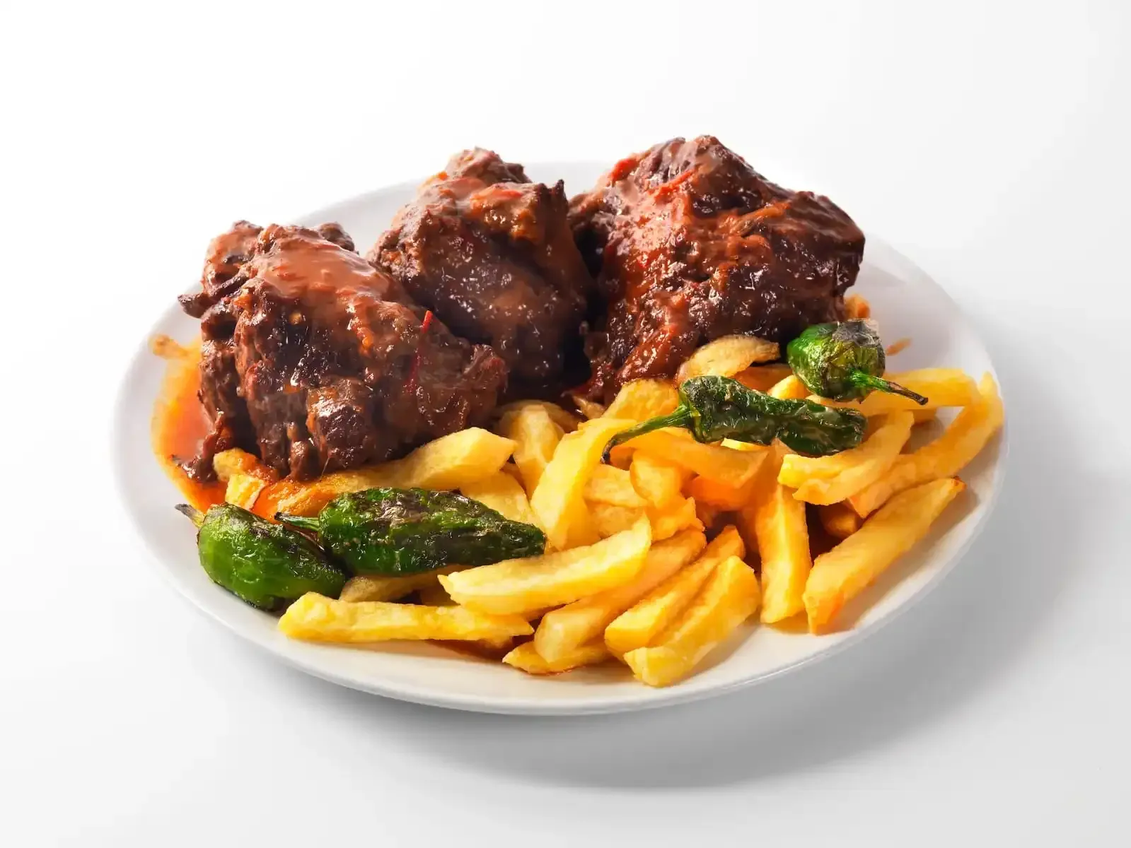 Plato de carne asada con patatas fritas doradas y calabacín sobre un fondo blanco.