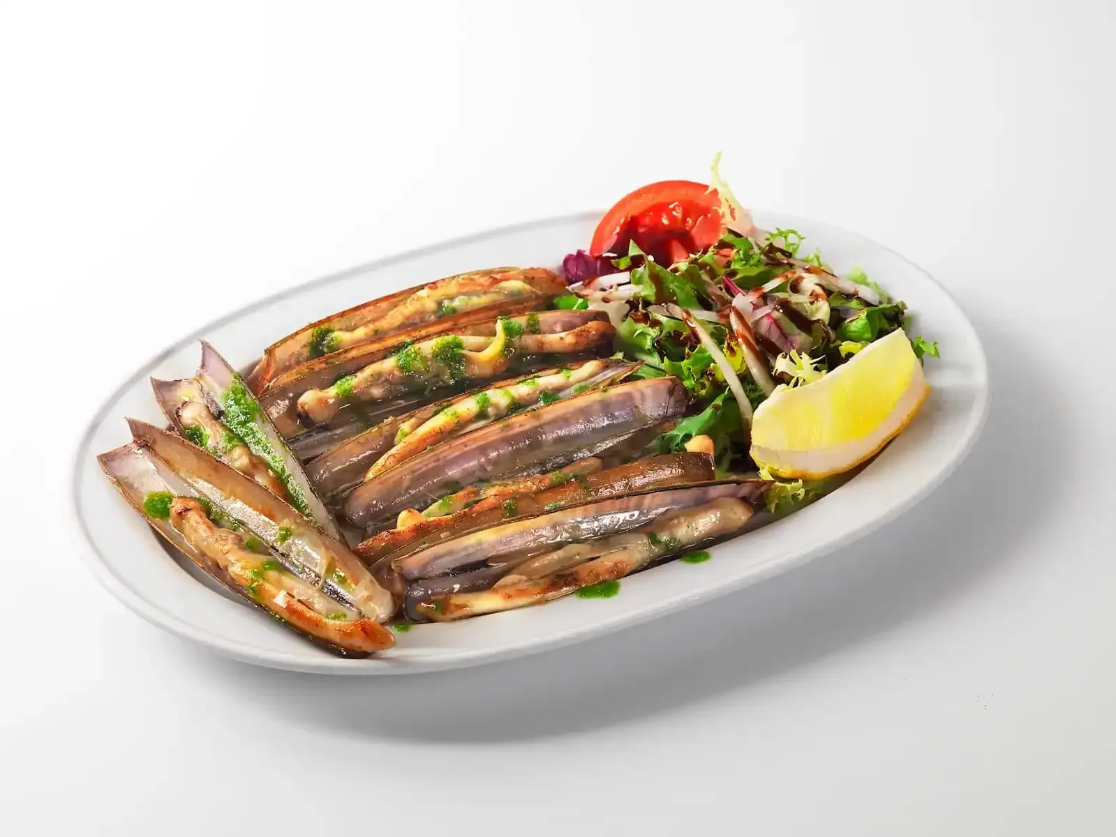 Filetes de pescado a la parrilla en un plato blanco con rodaja de limón, tomate y verduras.