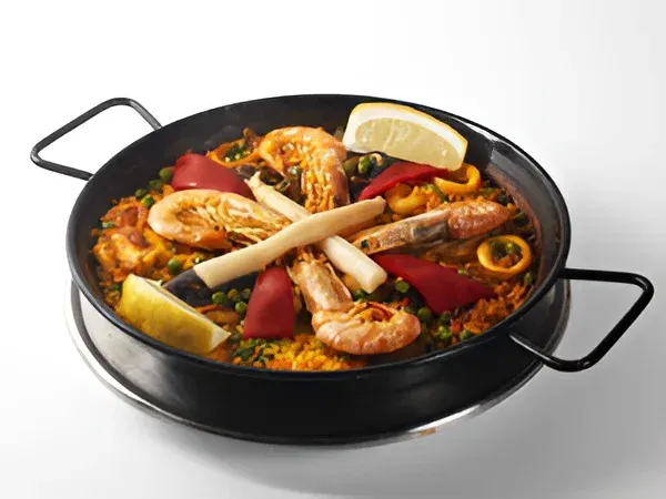 Paella en una sartén negra con gambas, arroz, pimientos y rodajas de limón.