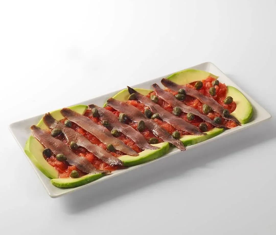 Postre de frutas emplatado con rodajas de kiwi, fresas y sirope de chocolate en un plato rectangular blanco.