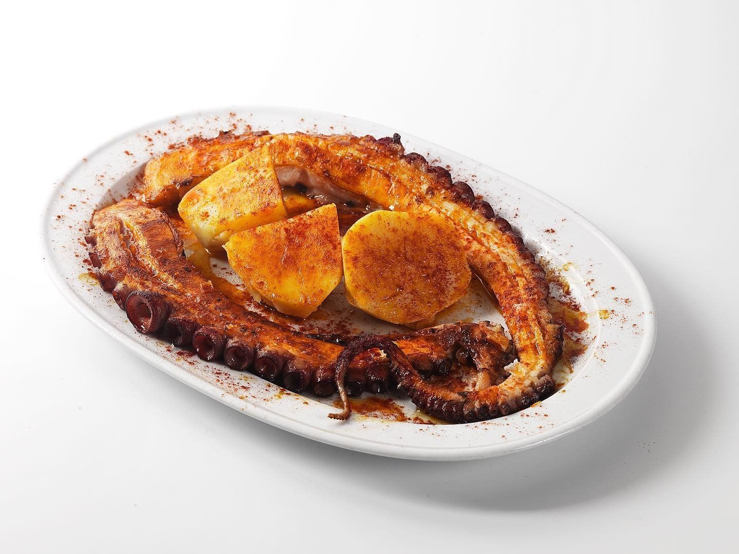 Pulpo a la plancha en un plato blanco con rodajas de limón y condimento de pimentón.