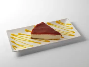 Una porción de tarta de queso bañada en salsa amarilla sobre un plato rectangular blanco.
