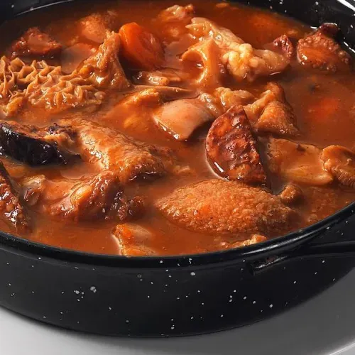 Bol de estofado rojo con carne y callos en un caldo oscuro.