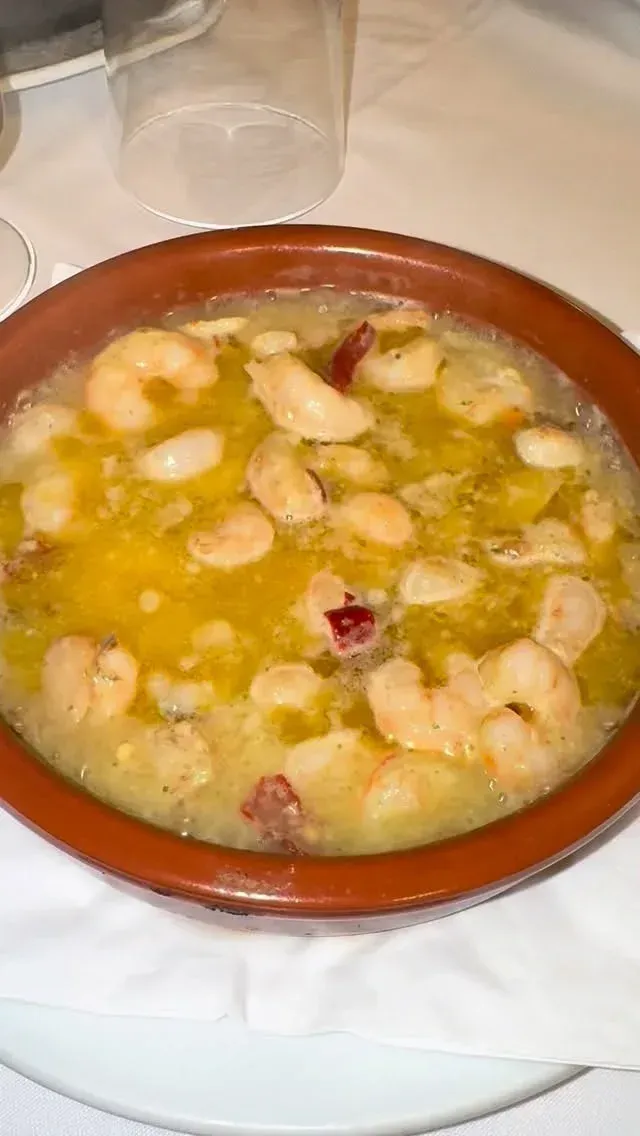 Un tazón de sopa o guiso amarillo cubierto con frijoles blancos sobre una mesa.