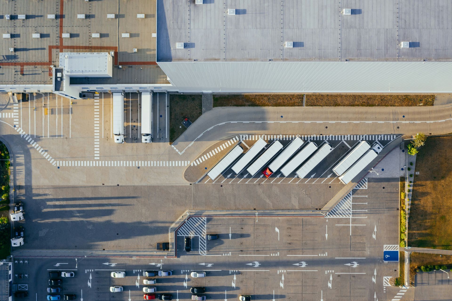 Vista aérea de una terminal de autobuses con autobuses blancos estacionados junto a un gran edificio y aparcamientos vacíos.