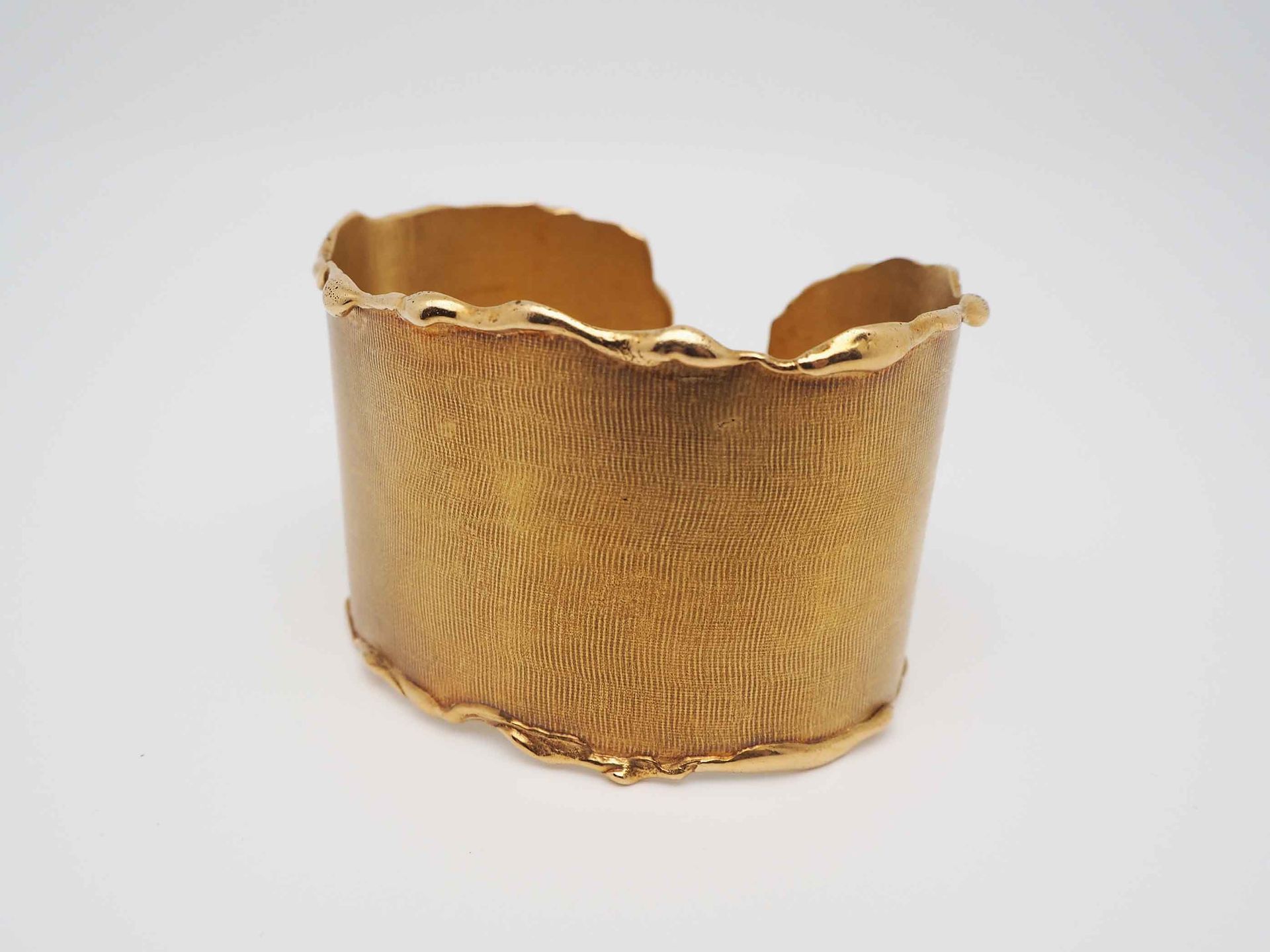 Un brazalete de oro reposa sobre una superficie blanca.