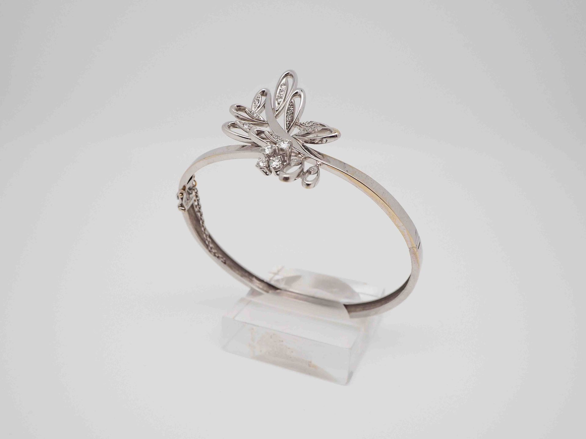 Una pulsera de plata con una mariposa está colocada sobre una superficie blanca.