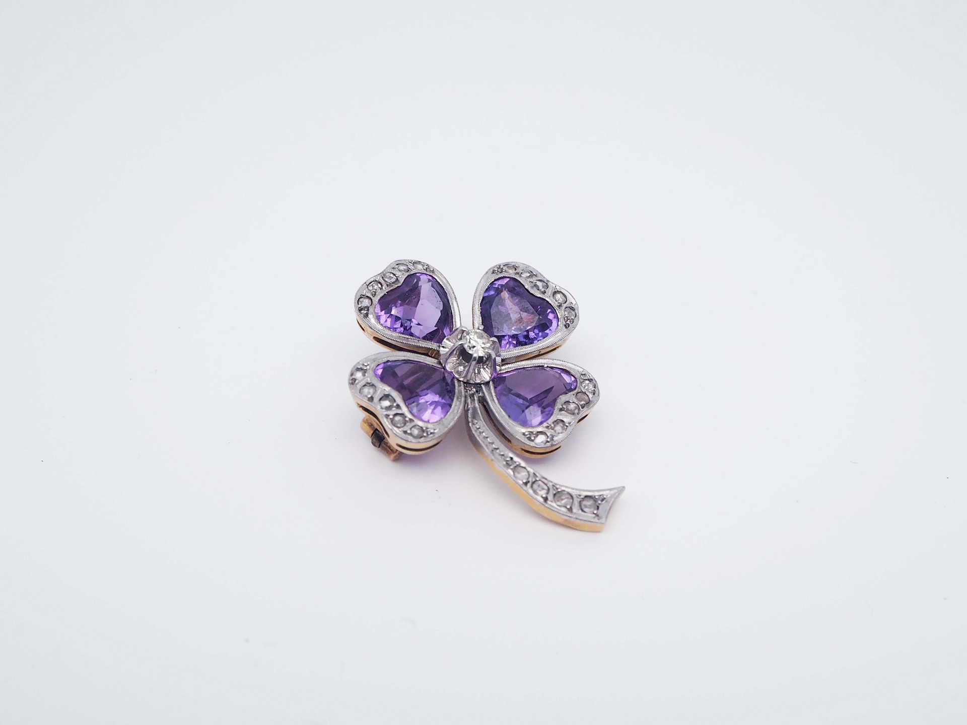 Un broche en forma de flor con piedras moradas y diamantes sobre fondo blanco.