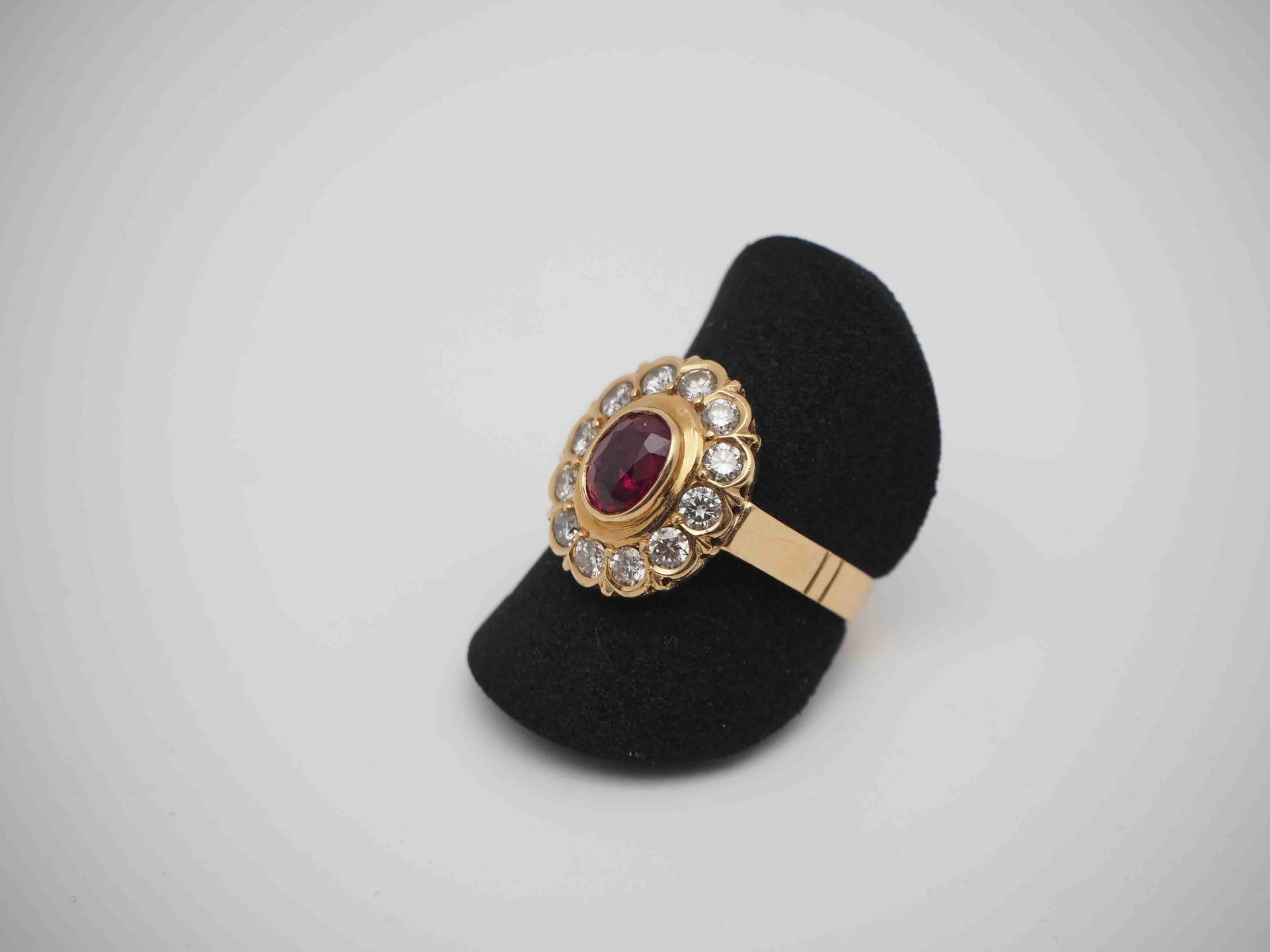 Un anillo de oro con un rubí y diamantes en un soporte de anillo negro.