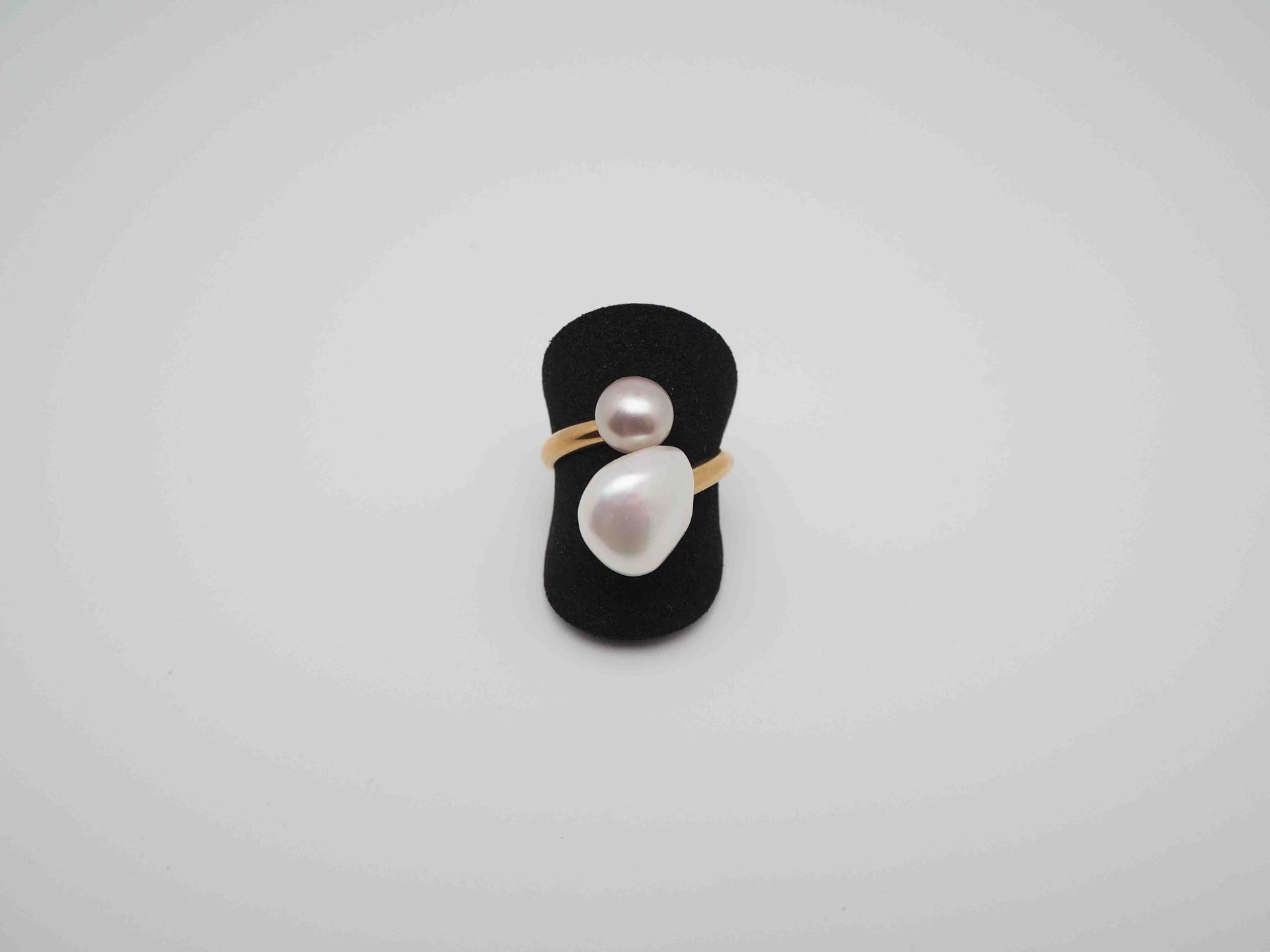 Un anillo con dos perlas en un soporte de anillo negro.