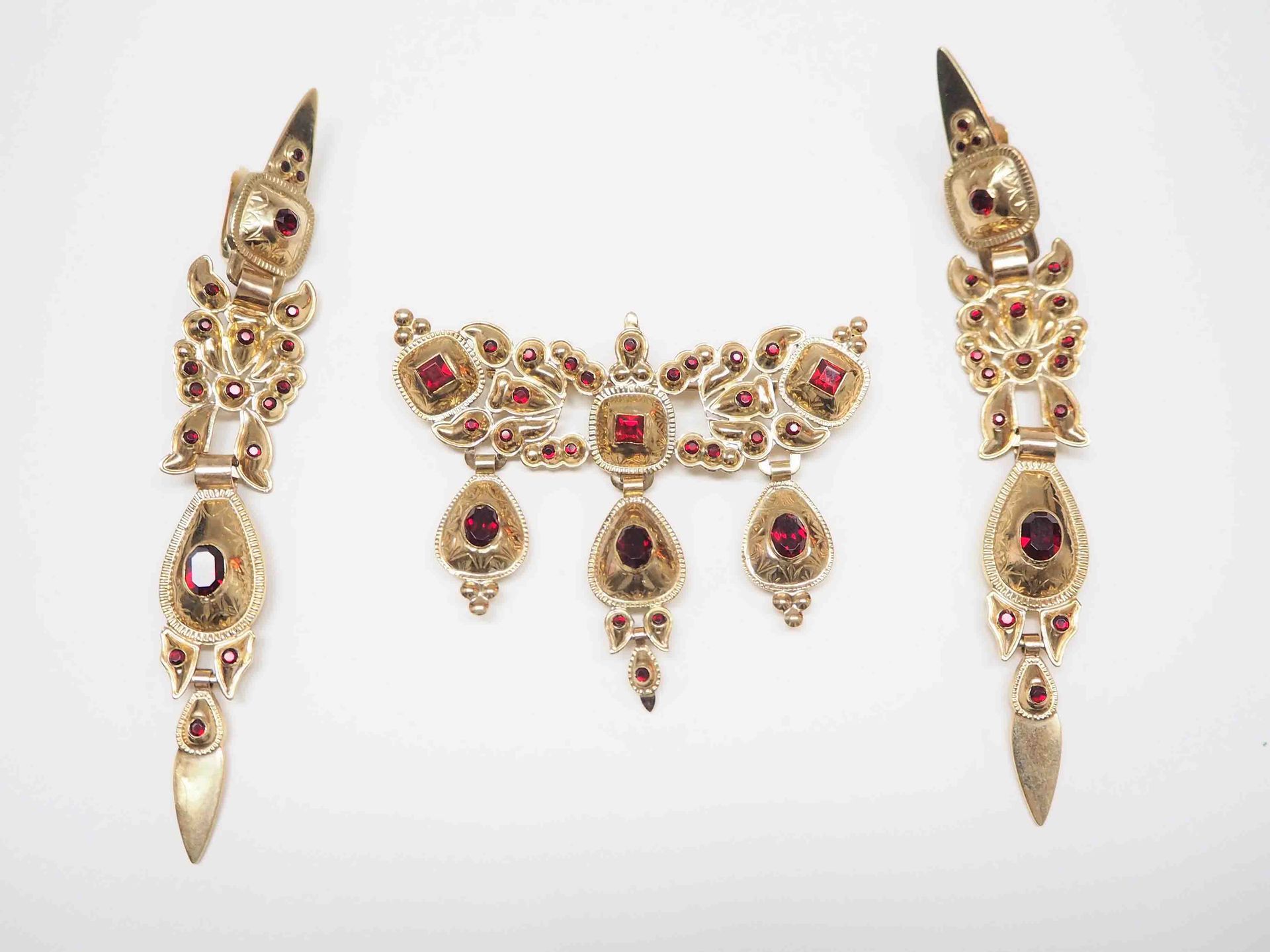 Un conjunto de joyas de oro con piedras rojas sobre un fondo blanco.