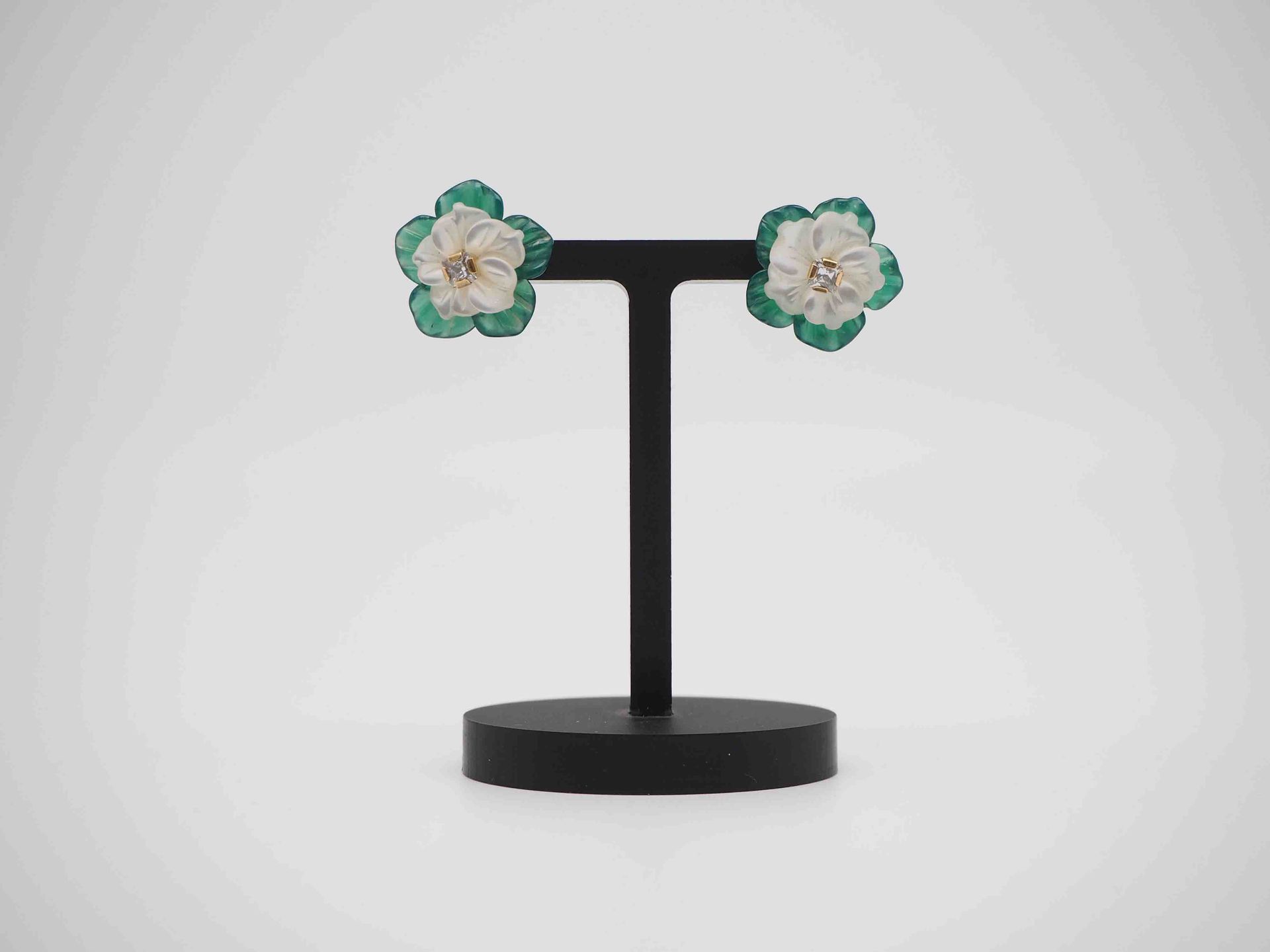 Un par de pendientes de flores verdes y blancas sobre un soporte negro.