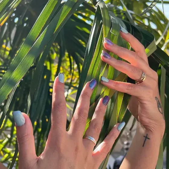 Una mujer con un tatuaje de cruz en el brazo sostiene una hoja de palmera.