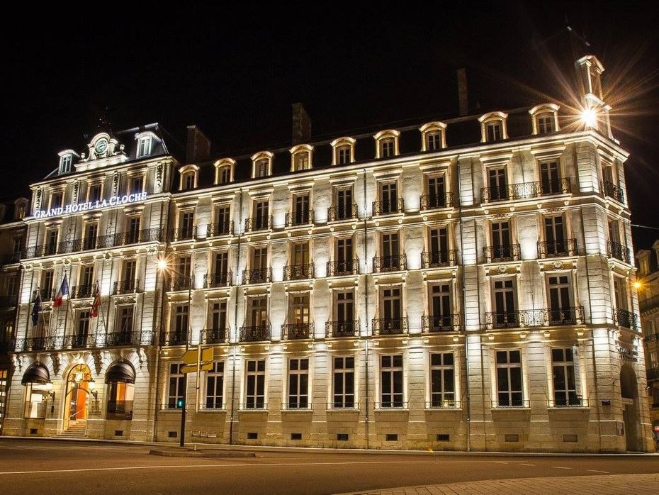 Immeuble de plusieurs étages illuminé la nuit, avec une façade ornée d'éclairages.