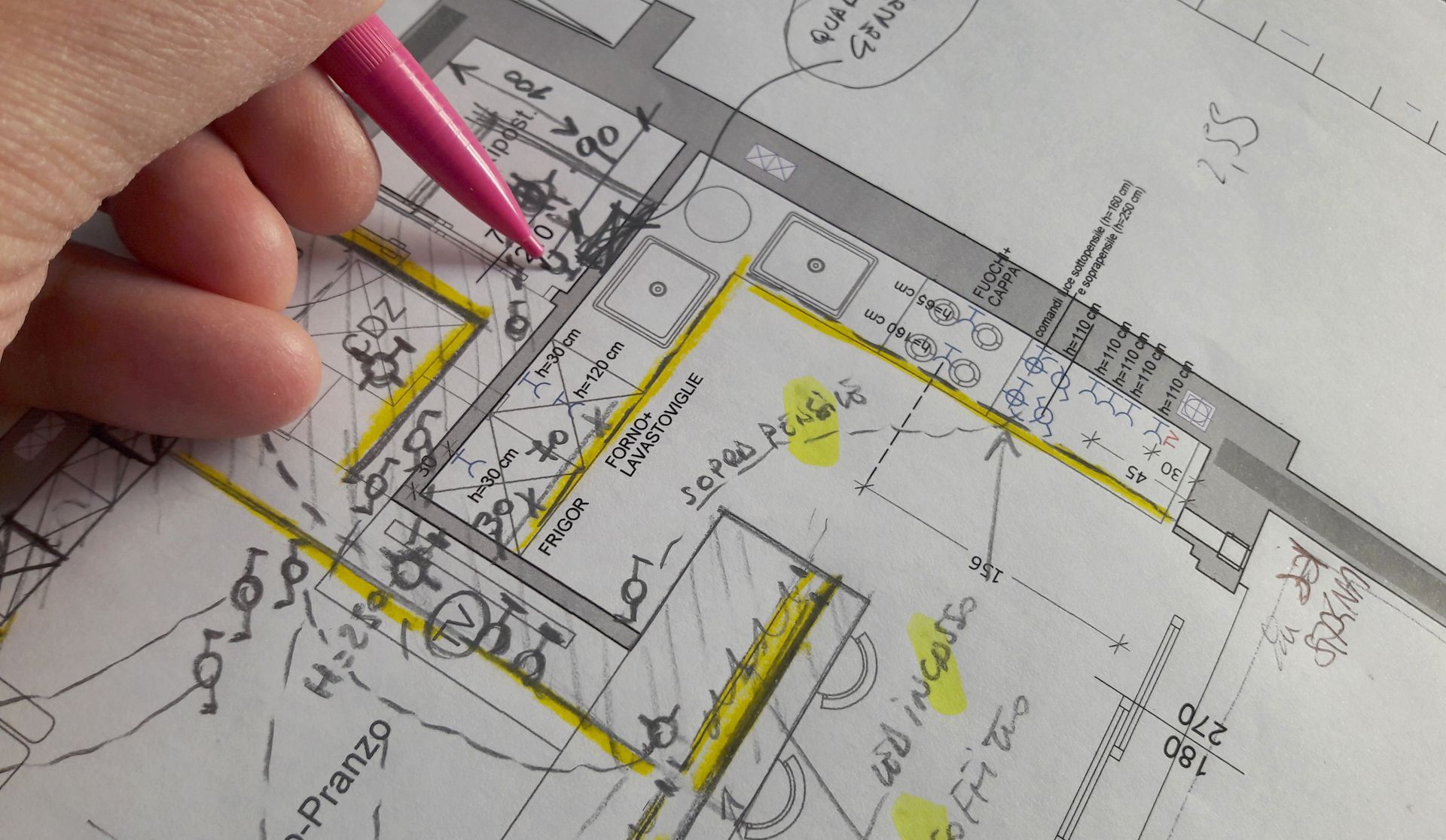 Une main utilise un stylo rose pour annoter un plan d'étage en papier, avec des surlignages jaunes.
