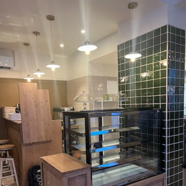 Un comptoir avec une vitrine dans une boulangerie, agrémenté d'éléments en bois et d'un mur carrelé d'un vert foncé brillant.