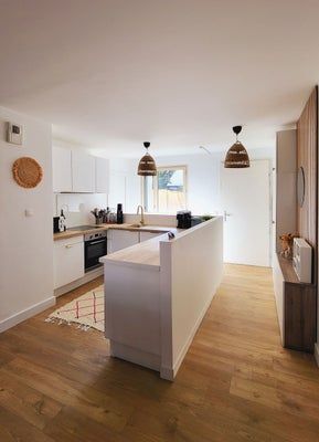 Cuisine blanche moderne avec parquet, îlot central et luminaires suspendus.