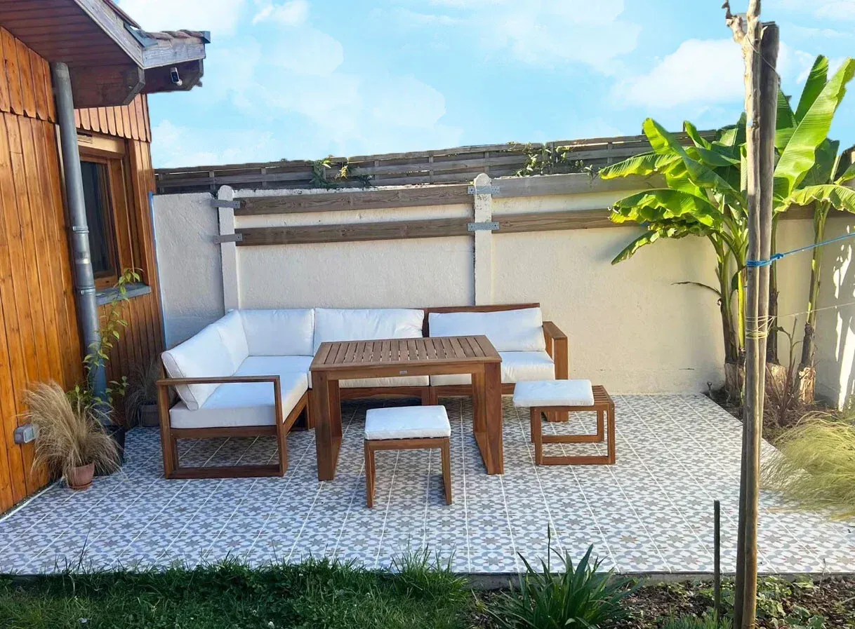 Coin salon extérieur avec mobilier en bois, coussins blancs et terrasse en pierre.