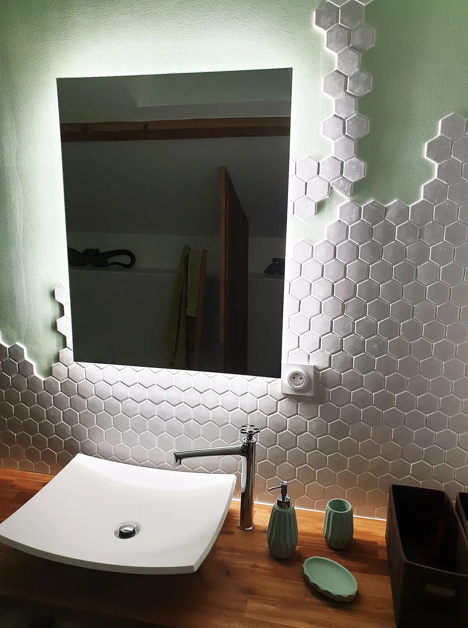 Salle de bains avec miroir entouré de lumières LED, carrelage blanc en nid d'abeille, vasque et comptoir en bois.
