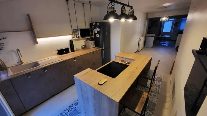 Cuisine moderne avec armoires et îlot en bois, électroménagers noirs, éclairage industriel.