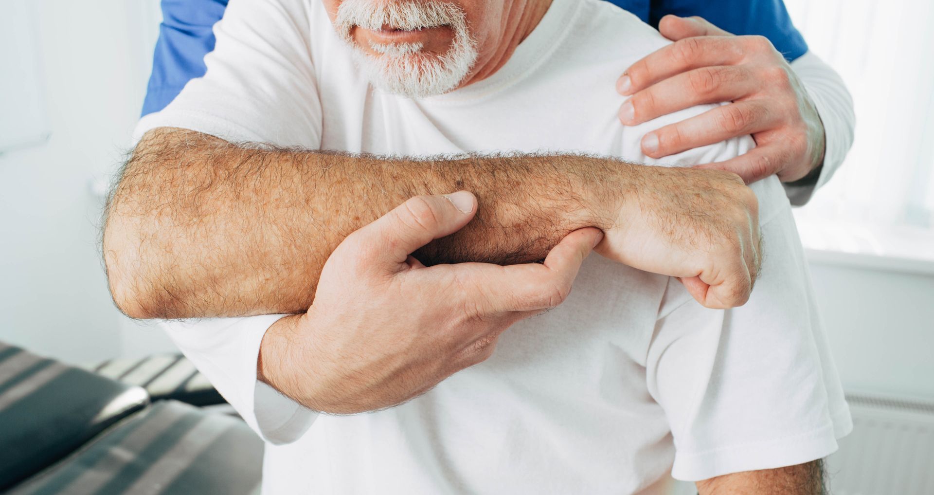 Un professionnel de la santé soutient le bras d'un homme âgé, peut-être pendant une thérapie physique, à l'intérieur.