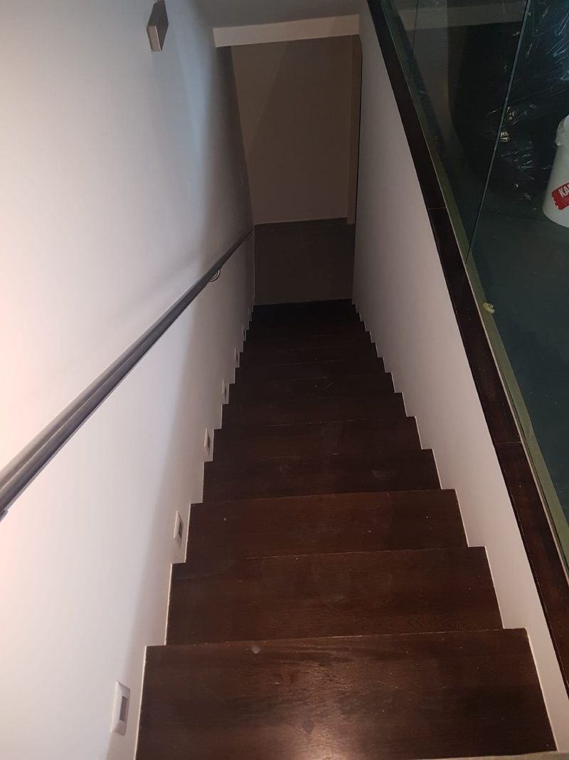 Un escalier en bois avec une rampe en verre et un mur blanc