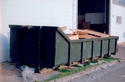 Un gran contenedor de basura está estacionado al costado de la carretera frente a un edificio.
