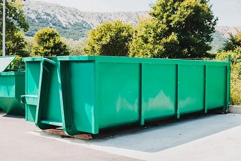 Un gran contenedor de basura verde está estacionado en un estacionamiento.