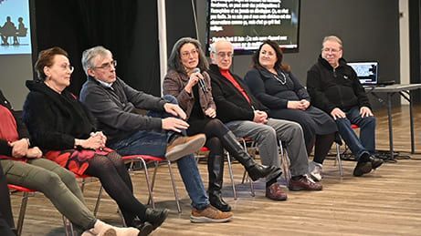 Six personnes sont assises sur des chaises rouges, probablement lors d'une table ronde, dans un cadre moderne avec un écran.