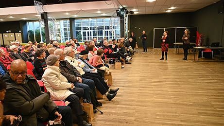 Dans une salle, deux femmes prennent la parole sur scène. Les spectateurs sont assis, ils écoutent et observent.