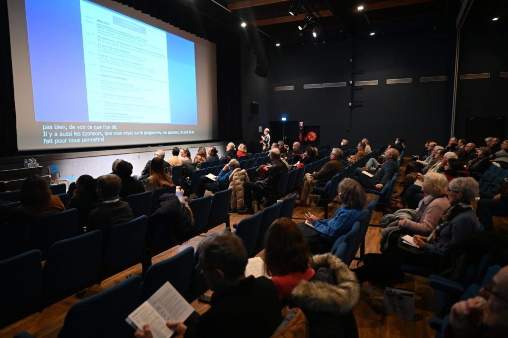 Le public regarde une présentation sur écran dans une salle de cinéma obscure.