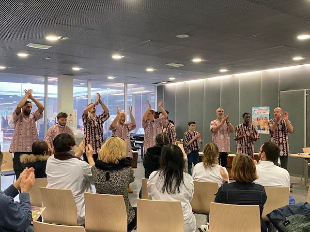 Un groupe de personnes applaudit dans une pièce moderne, tandis qu'un groupe d'artistes porte des chemises assorties.