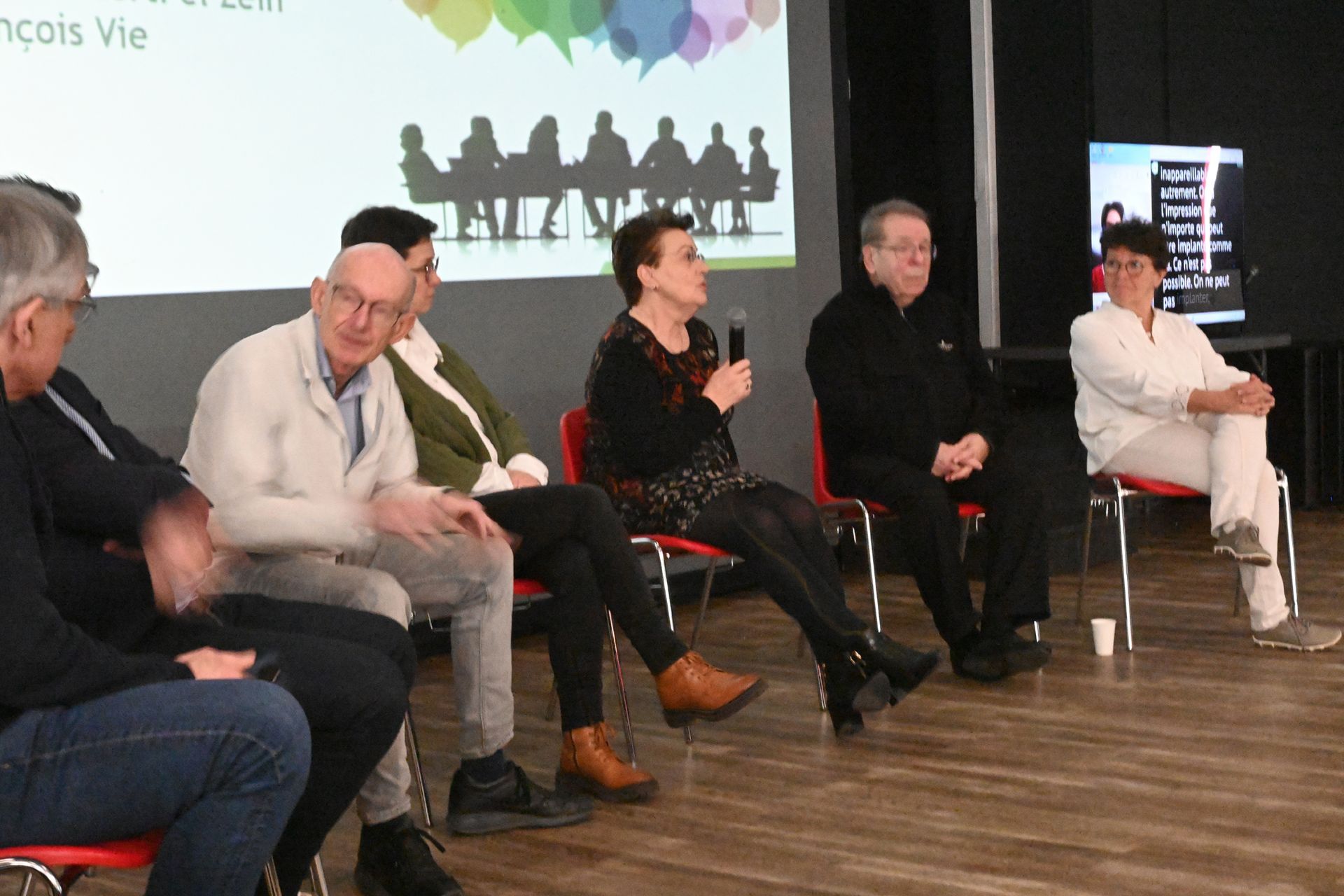 Discussion avec cinq intervenants assis sur scène, dont l’un tient un micro devant un écran de projection