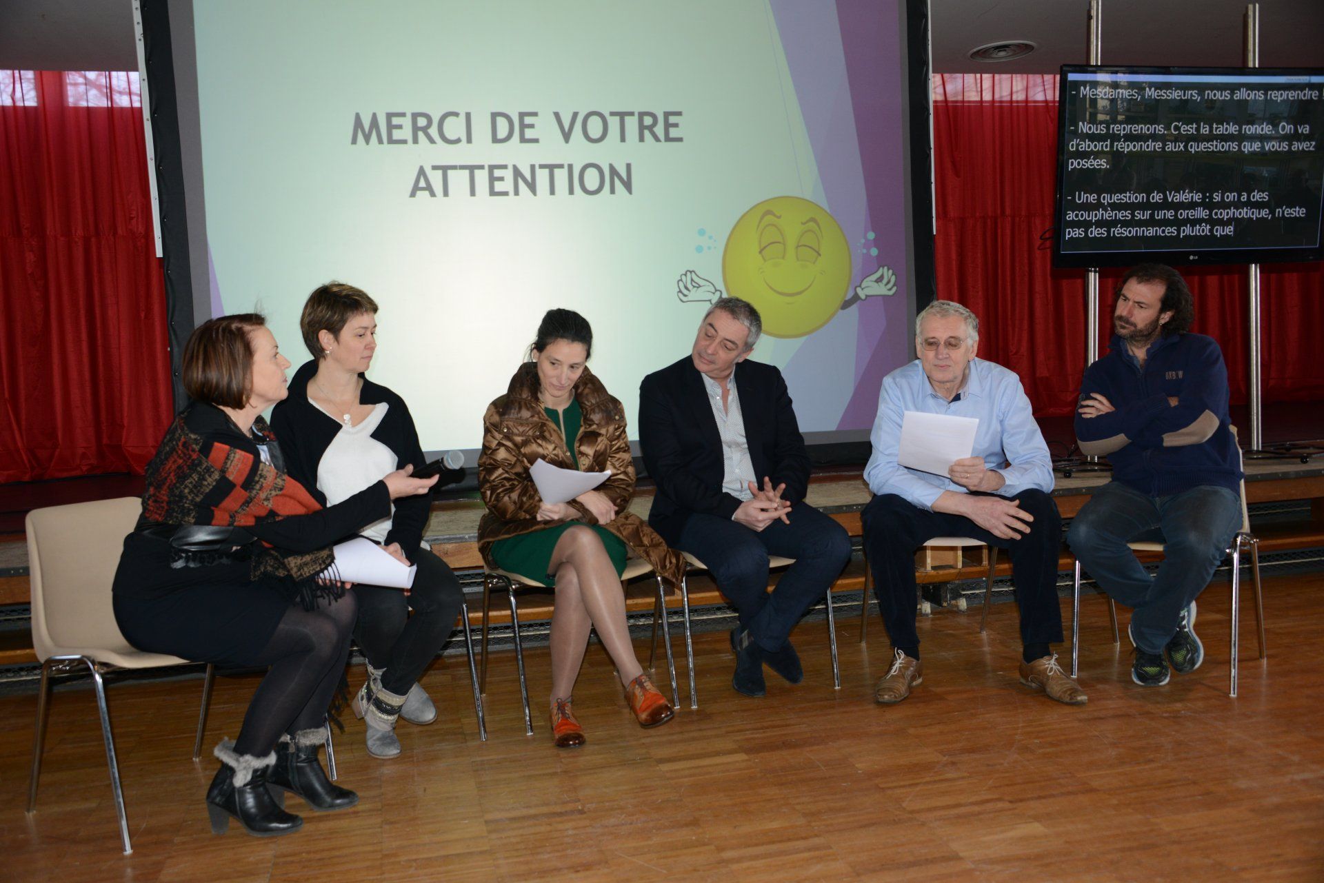 Un groupe est assis sur des chaises, certains tenant des papiers, face à un écran sur lequel est inscrit « MERCI DE VOTRE ATTENTION ».