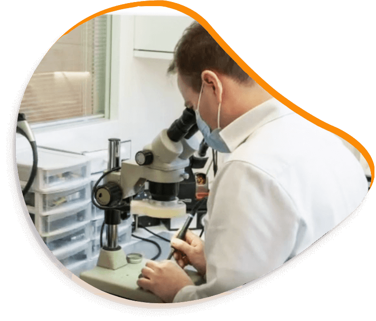 Une personne en blouse blanche et masque regarde au microscope dans un laboratoire, en train d'écrire.