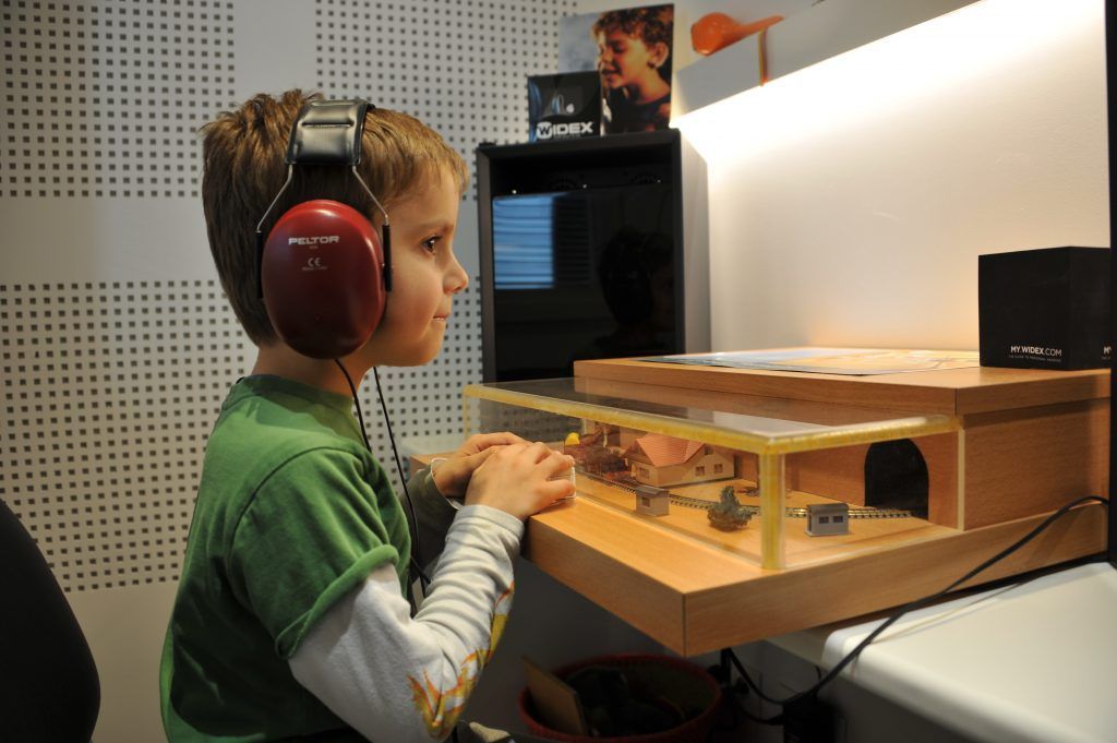 Un garçon portant un casque audio, concentré sur une console audio en bois recouverte d'un plastique transparent, dans un studio.