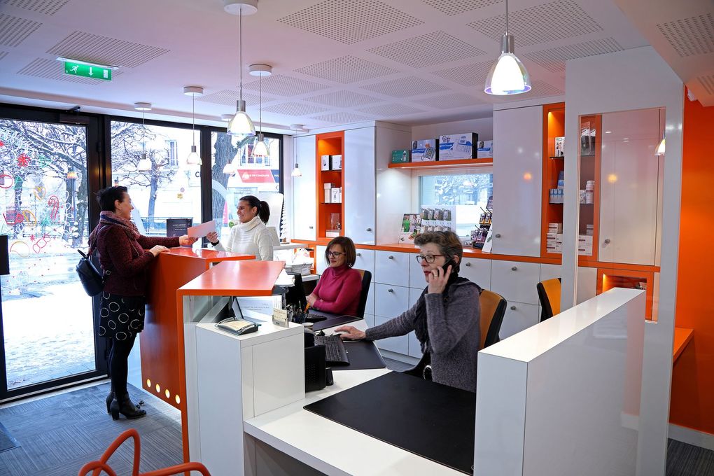 Intérieur d'un bureau : personnes à l'accueil ; décor orange et blanc. Une femme au téléphone.