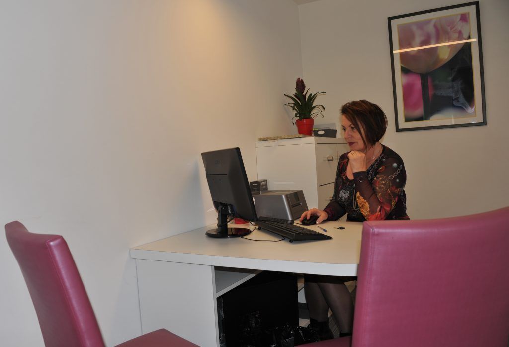 Femme travaillant sur un ordinateur dans un bureau, face à l'écran, chaises roses.