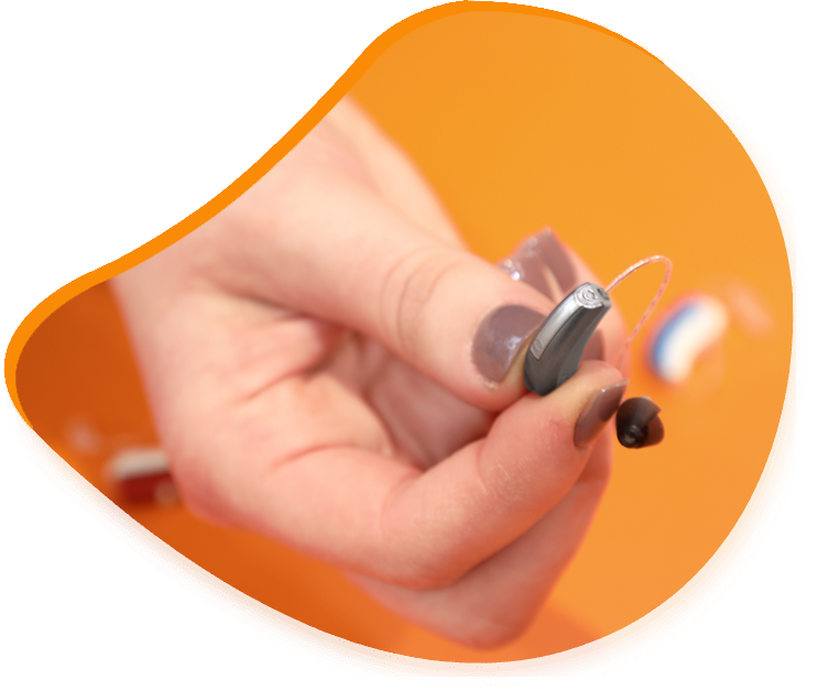 Main tenant un petit appareil auditif gris et un embout auriculaire sur fond orange.