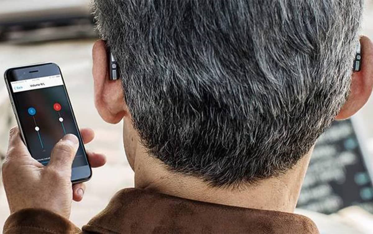 Personne portant des appareils auditifs, ajustant les paramètres d'un smartphone.