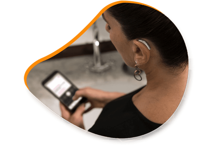 Une femme utilise un smartphone, portant un appareil auditif, près d'un évier.