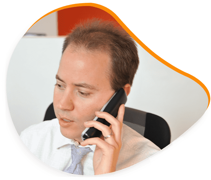 Un homme en chemise blanche et cravate parle au téléphone, regardant vers la gauche.