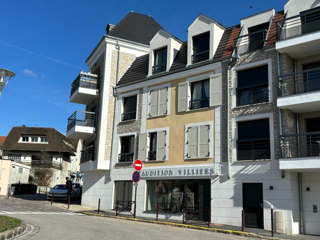 Immeuble avec un magasin, des appartements avec balcon et une route par une journée ensoleillée.