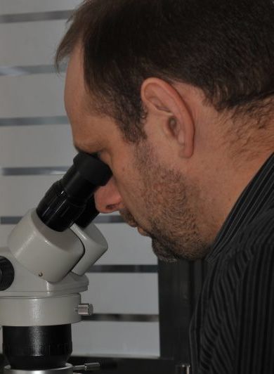 Un homme observe un instrument au microscope, gros plan. Il porte une chemise sombre et se concentre sur l'équipement d'un laboratoire.