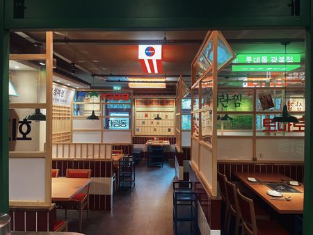 Empty Korean-style restaurant interior with red booths, wooden tables, and neon signs.