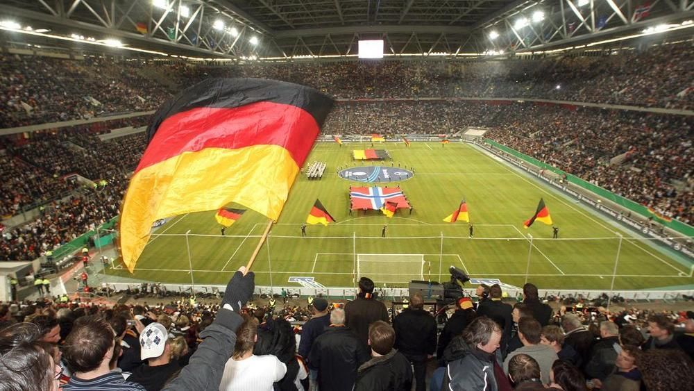 Soccer stadium packed with fans waving large German flags during a match ceremony